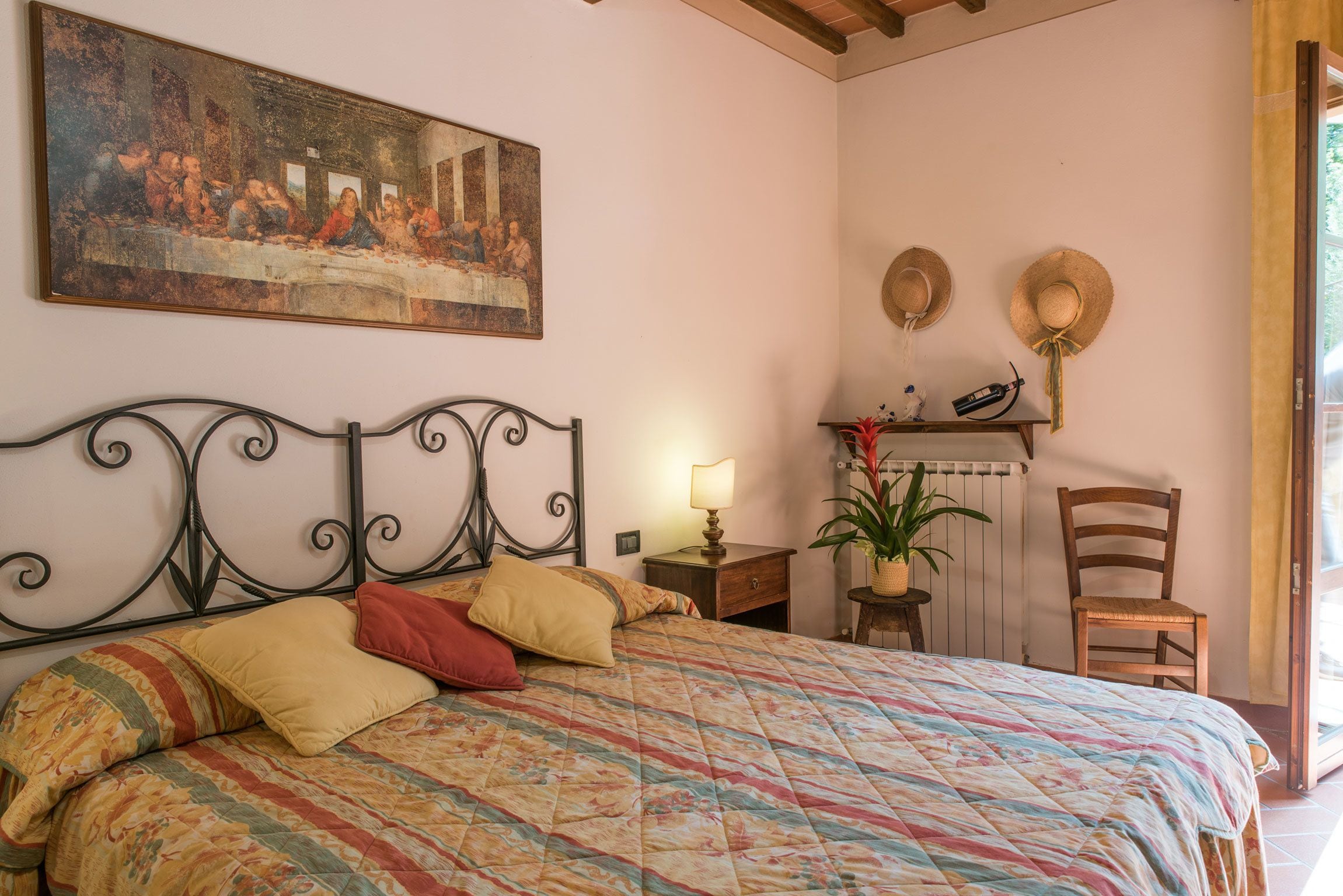 A bedroom with a bed, a painting, a lamp, a chair, and a small table.