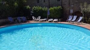 A swimming pool with lounge chairs and umbrellas, surrounded by stone walls and greenery. - Podere Poggetto (Barberino Tavarnelle)