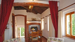 A dining area with a brick fireplace, wooden dining table, and floral-patterned chairs. - Podere Poggetto (Barberino Tavarnelle)