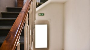 A staircase with a wooden handrail leading to a door with a green exit sign. - Hotel Bella Firenze (Florence)
