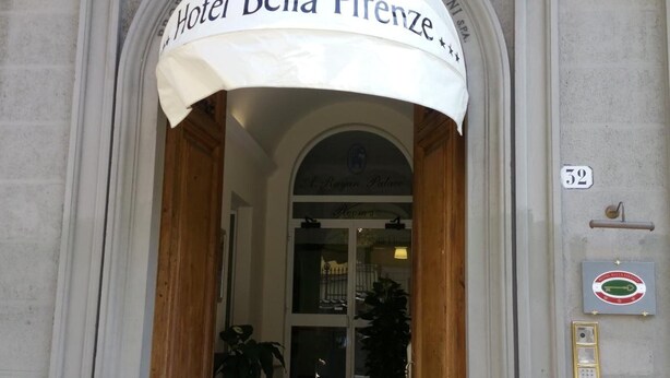 The entrance to Hotel Bella Firenze with a classic arched doorway, a sign above the door, and a doormat with the hotel's initials. - Hotel Bella Firenze (Florence)