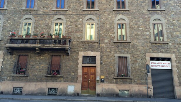 Un edificio de varios pisos de piedra con ventanas arqueadas, una puerta de madera y un balcón con macetas.