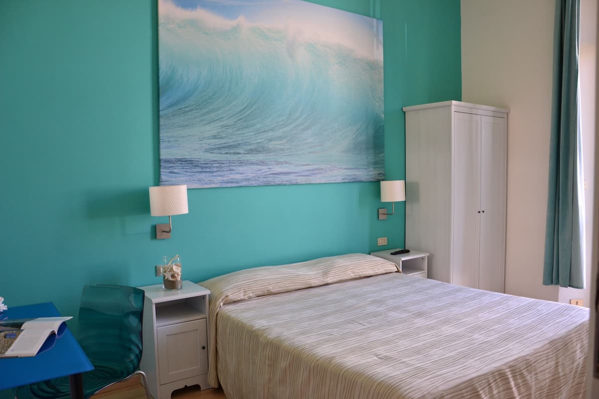 A bedroom with a bed, nightstands, a lamp, a cabinet, and a painting of a wave on the wall.