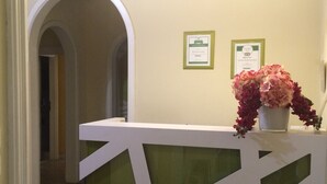 Un mostrador de recepción con diseño geométrico, una planta en maceta y dos certificados enmarcados en la pared.