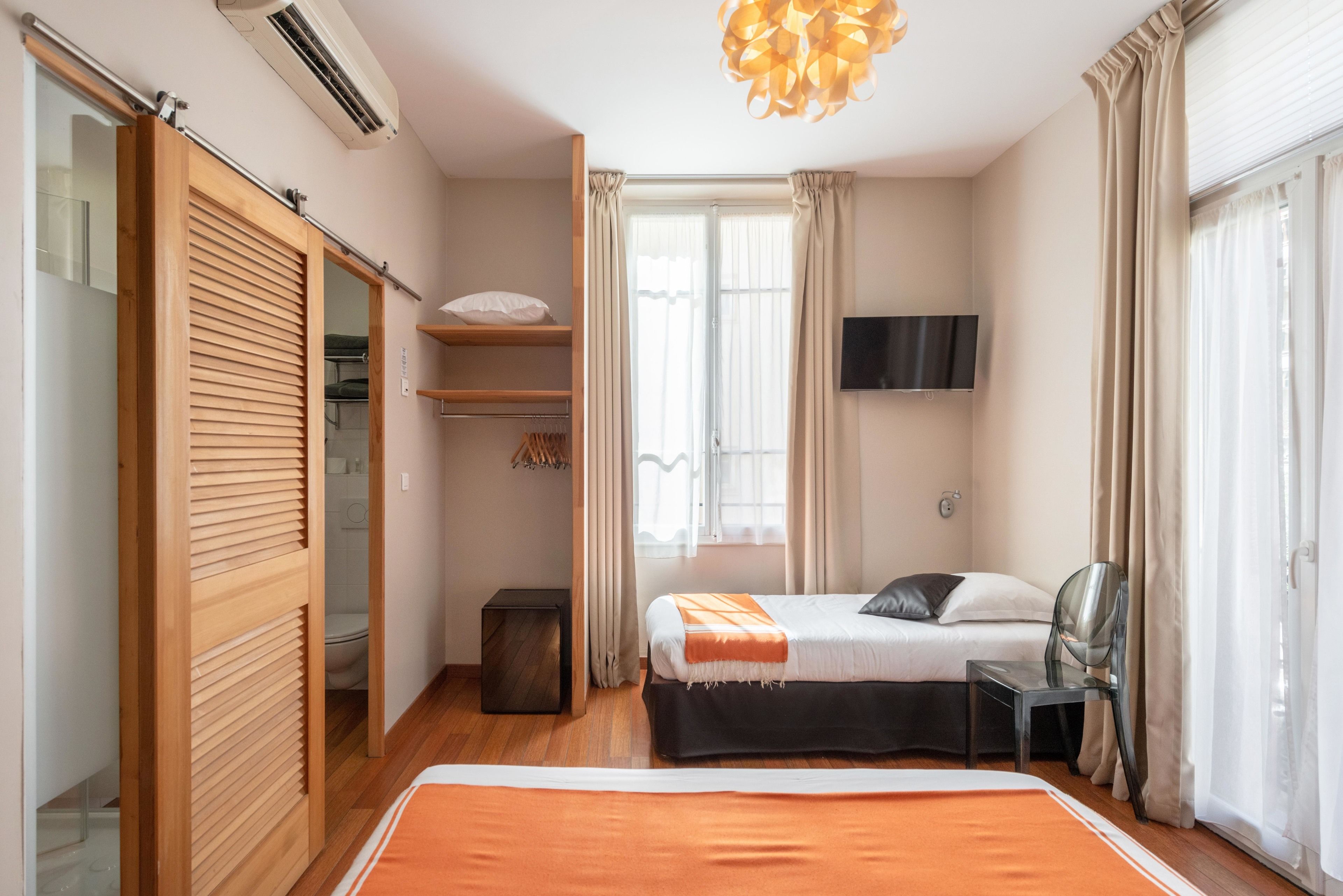 Un dormitorio con cama, televisor, sillón y ventana con cortinas.