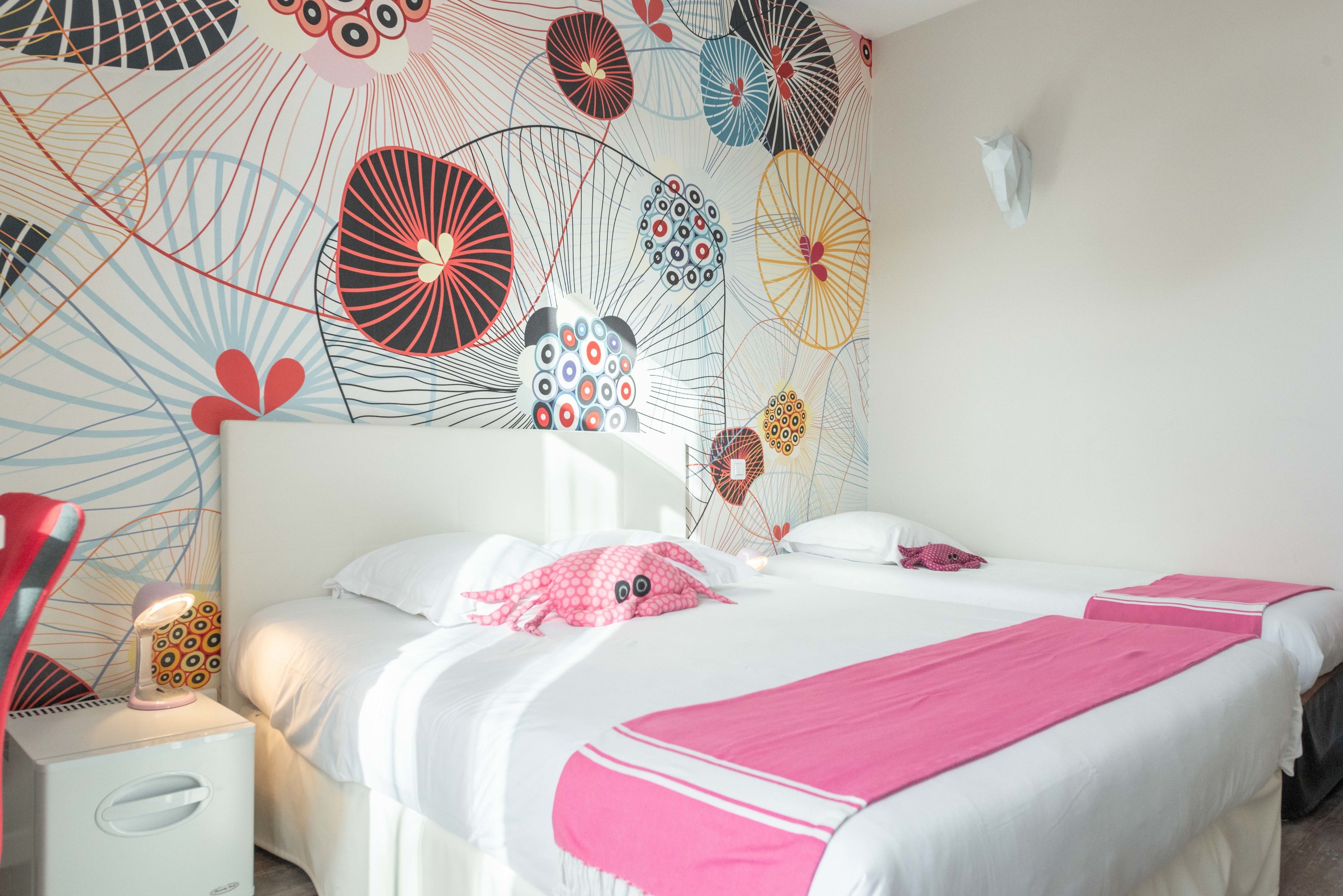 A hotel room with a bed, a nightstand, a lamp, and a wall with a colorful abstract design.
