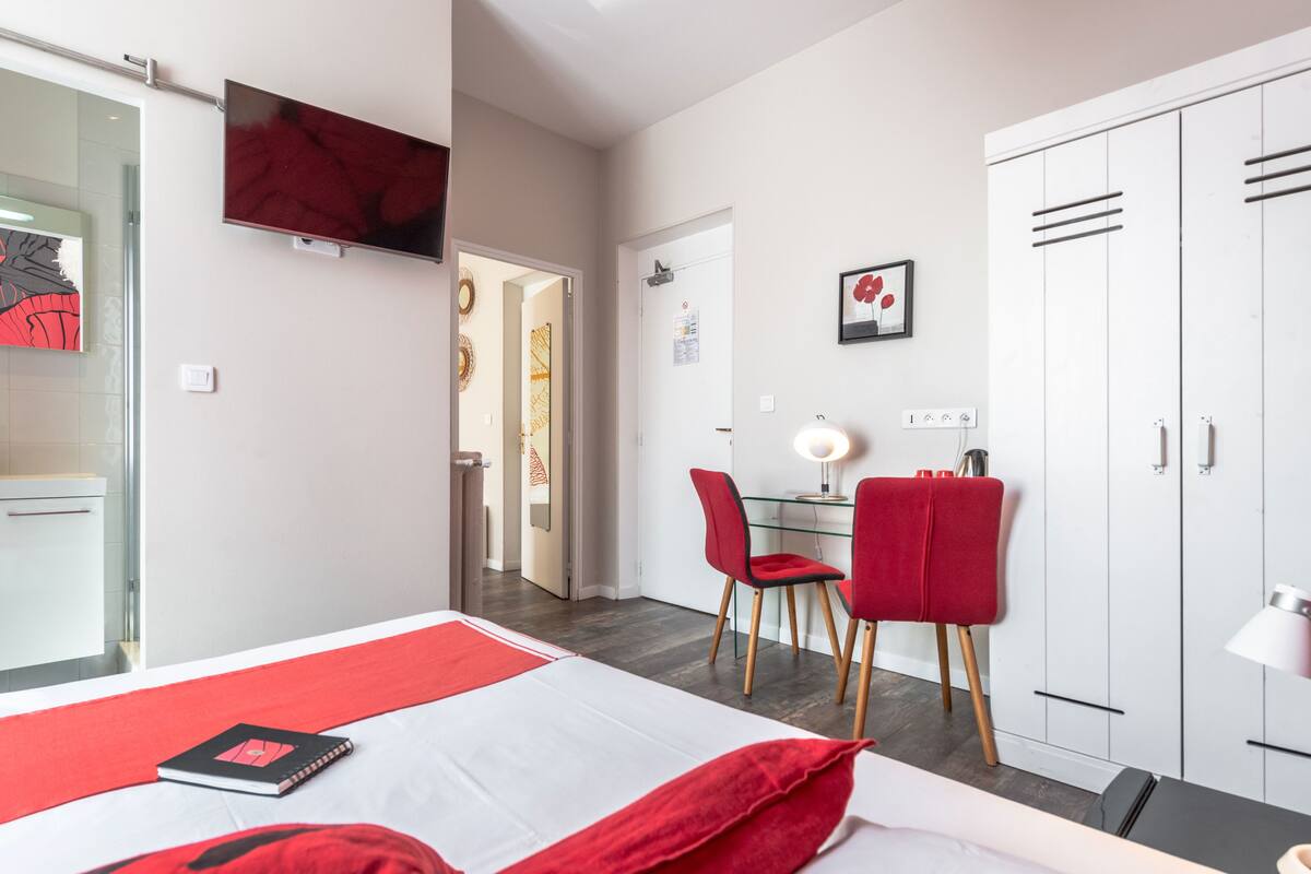 Habitación de hotel con cama, escritorio, silla, televisor montado en la pared y armario.