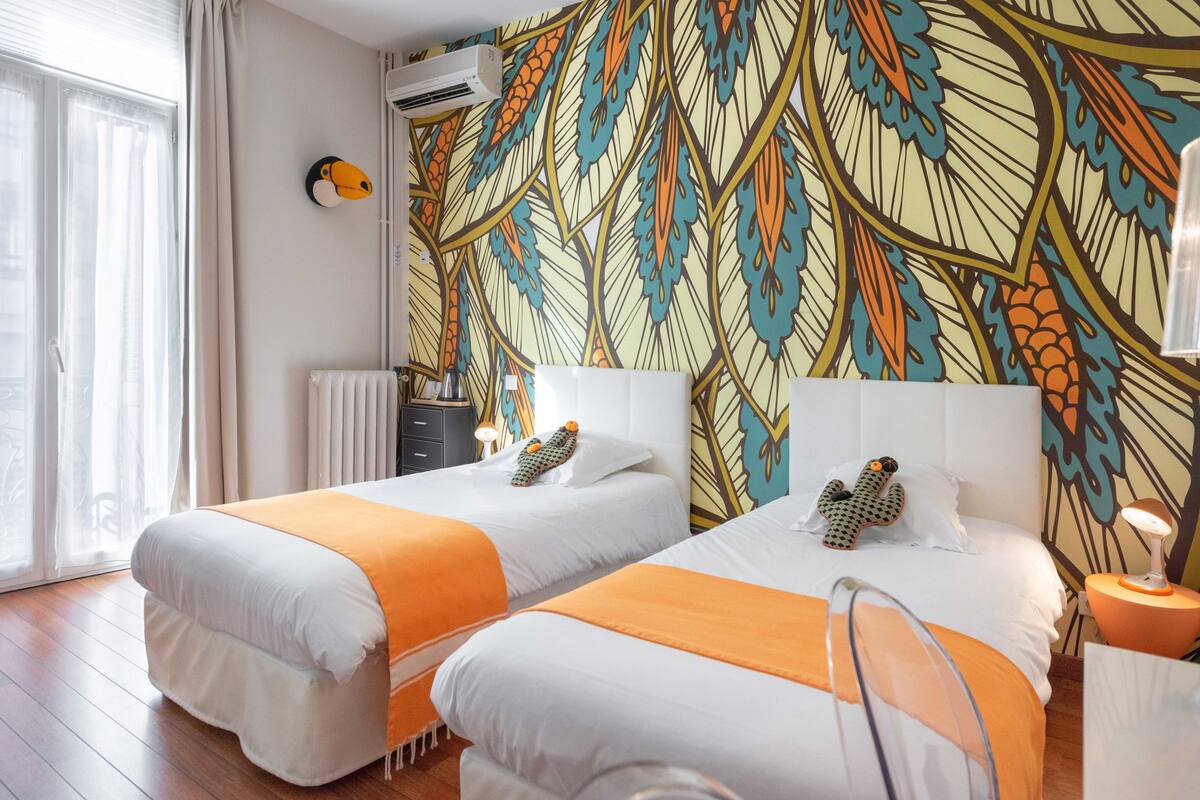 Habitación de hotel con dos camas, un radiador, una ventana con cortinas y una pared con un diseño de hojas.
