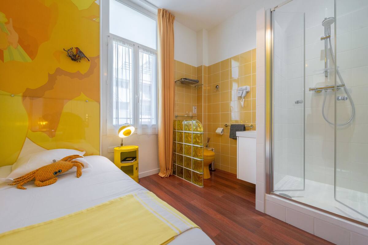Una habitación de hotel con cama, baño con ducha y ventana con cortinas.