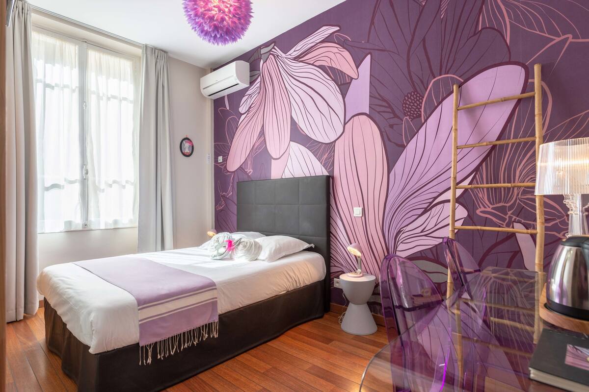 Un dormitorio con cama, mesita de noche, lámpara, aire acondicionado de pared y ventana con cortinas.