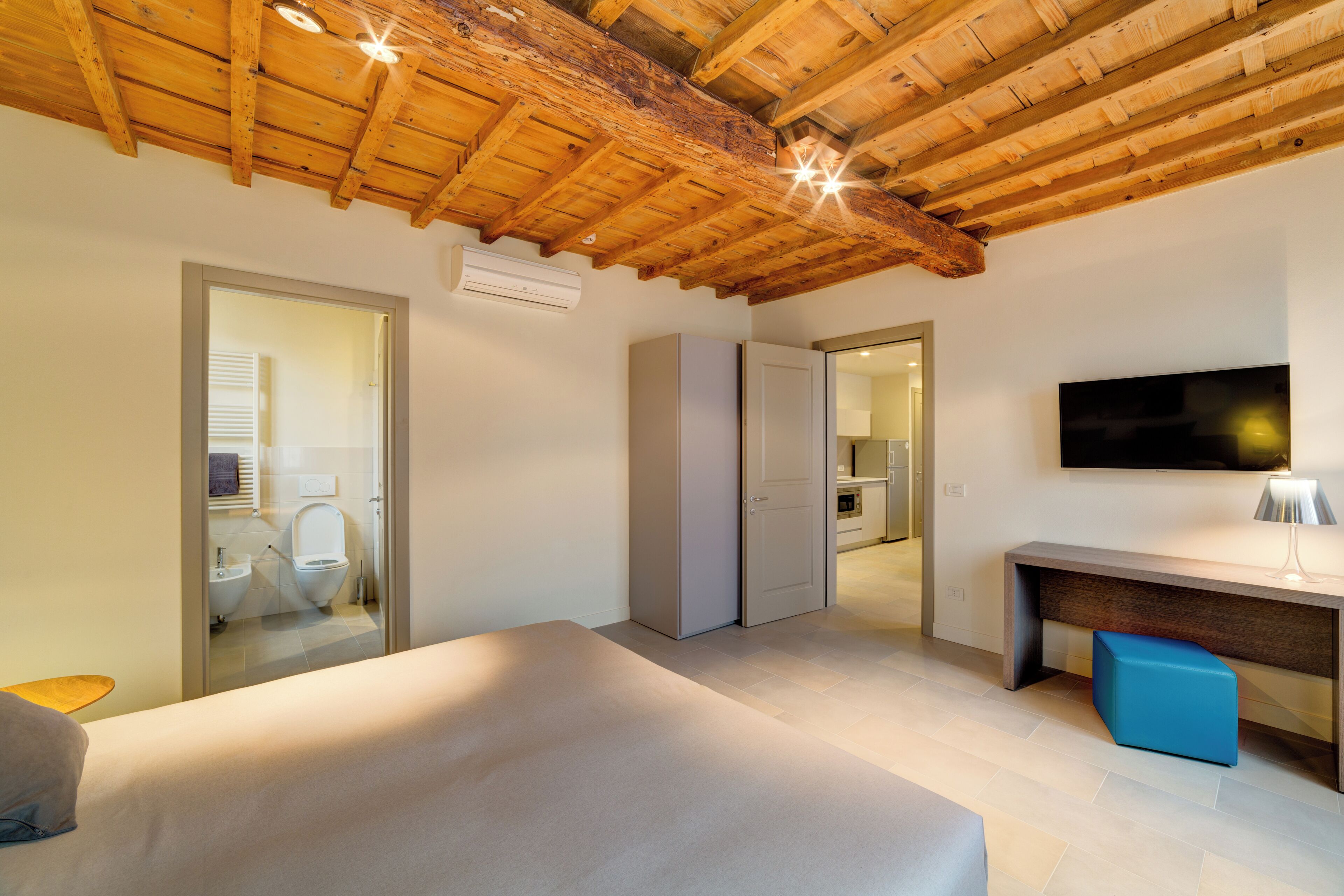 A bedroom with a wooden ceiling, a bed, a desk, and a TV.