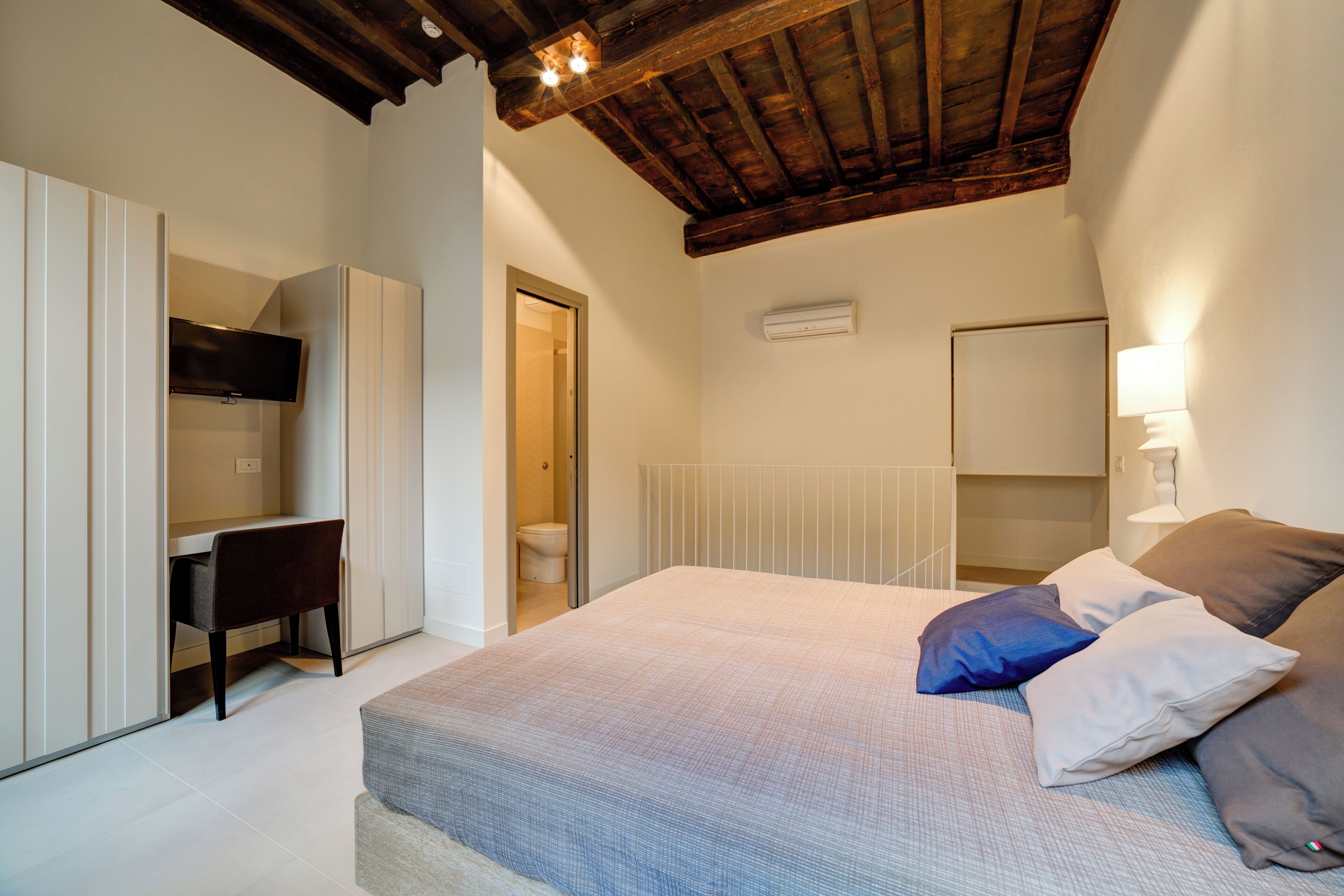 Un dormitorio con cama, almohadas, escritorio y televisor.