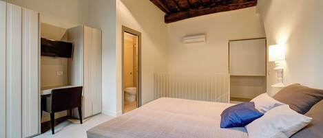 Un dormitorio con cama, almohadas, escritorio y televisor.