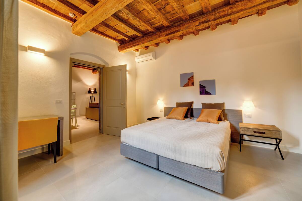 Ein Schlafzimmer mit Bett, Nachttischen, einem Schreibtisch und einer Tür zu einem anderen Raum.