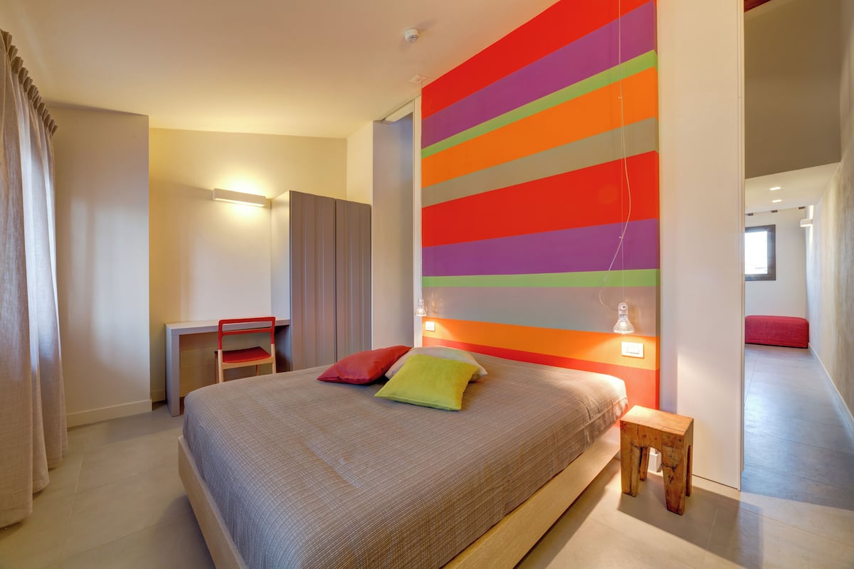 Ein modernes Schlafzimmer mit einem großen Bett, einem Schreibtisch und einer lebhaften, gestreiften Wand.