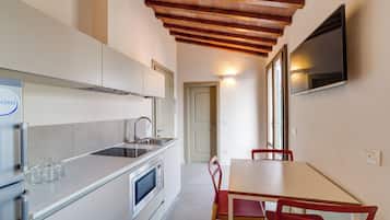 A modern kitchen with a built-in oven, microwave, and sink. There is a dining table with red chairs and a TV mounted on the wall.