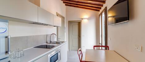 Una cocina moderna con horno empotrado, microondas y lavaplatos. Hay una mesa de comedor con sillas rojas y un televisor montado en la pared.
