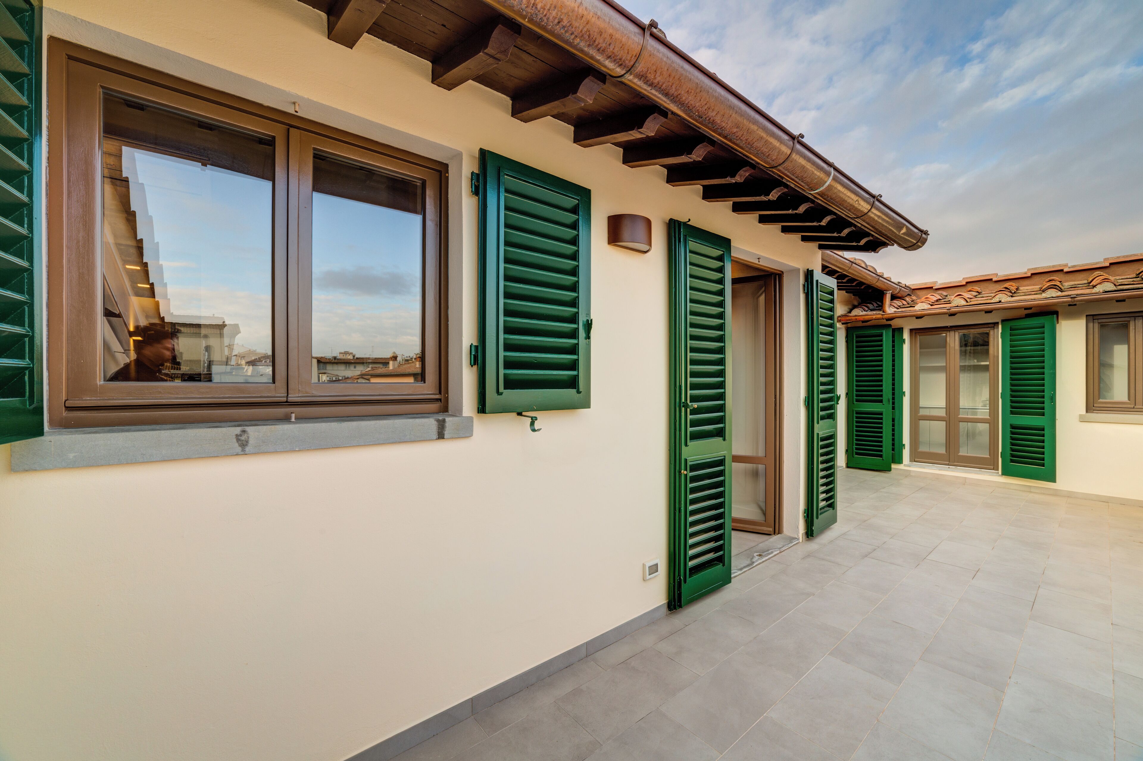 A building exterior with a tiled floor, green shutters, and a visible staircase.