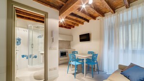 A modern interior with a glass shower, wooden ceiling beams, a dining area with blue chairs, and a sofa with cushions.