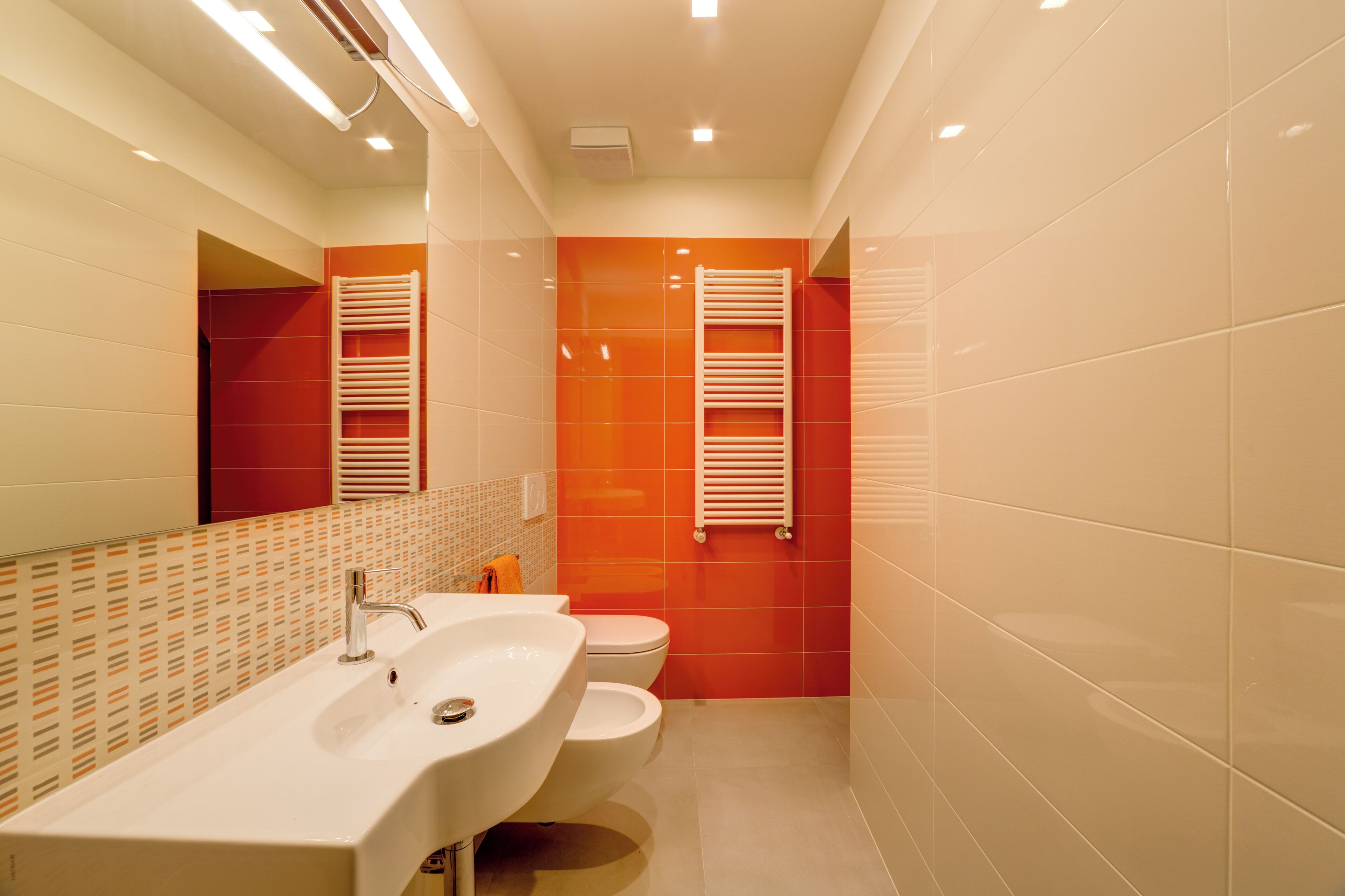 A modern bathroom with a large sink, toilet, and two towel racks.