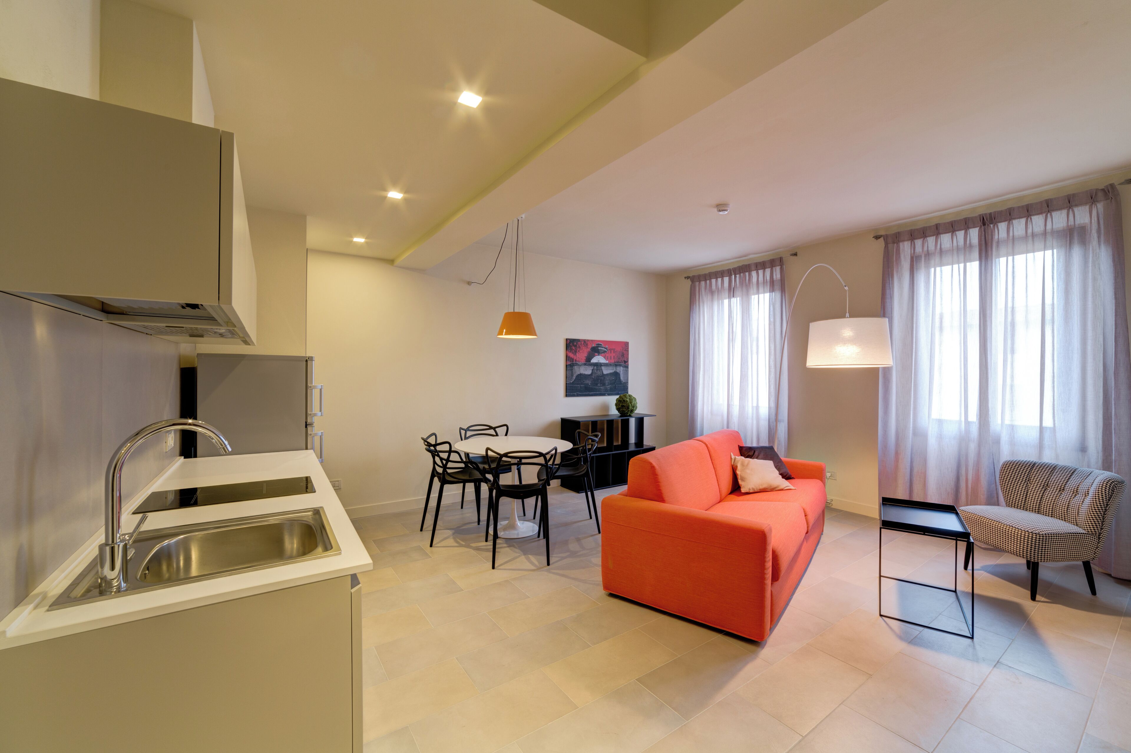 A modern kitchen with a built-in sink, dining area with chairs, a sofa, and a chair.