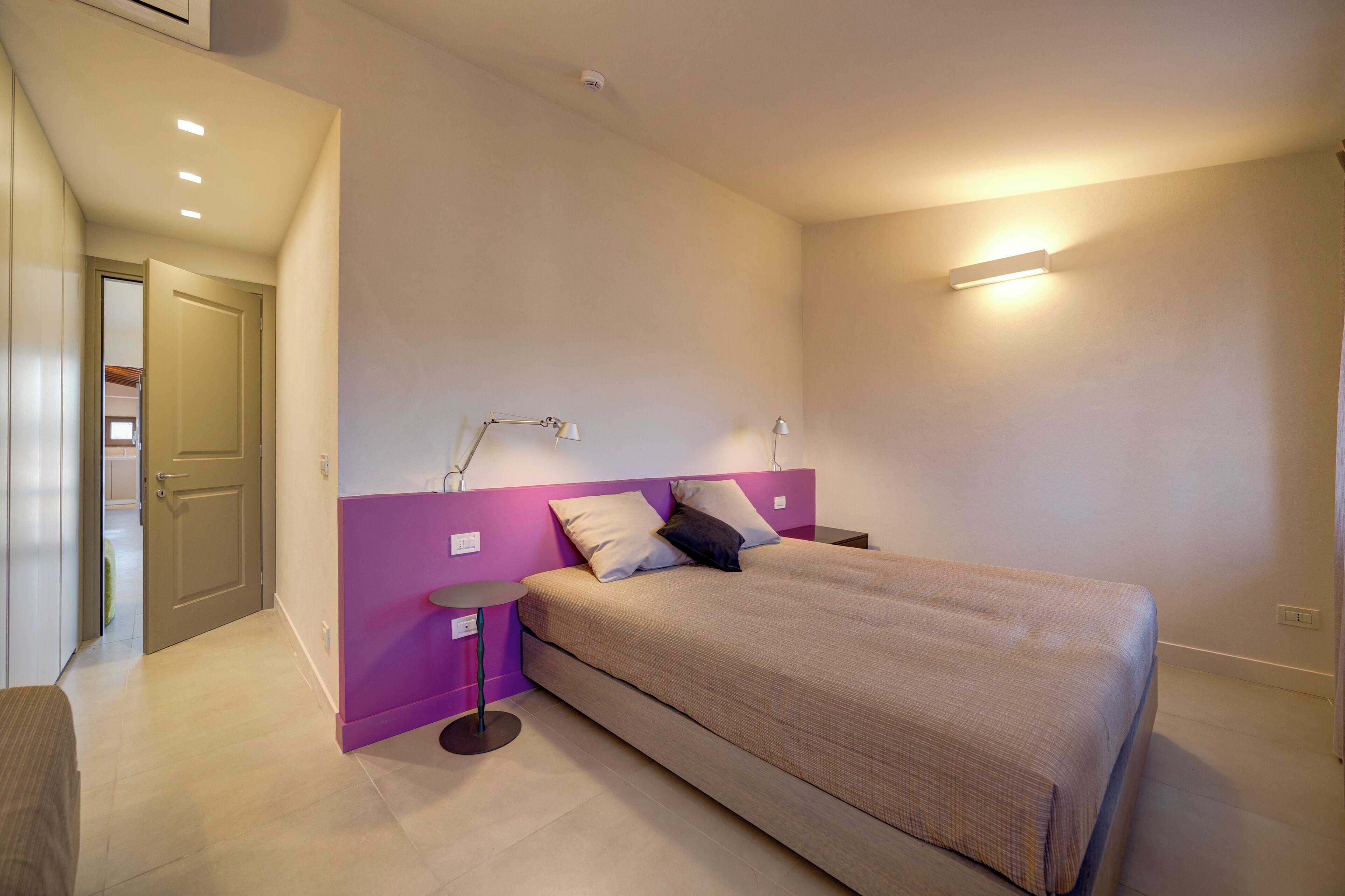A bedroom with a bed, a bedside table, a lamp, and a wall-mounted light fixture.