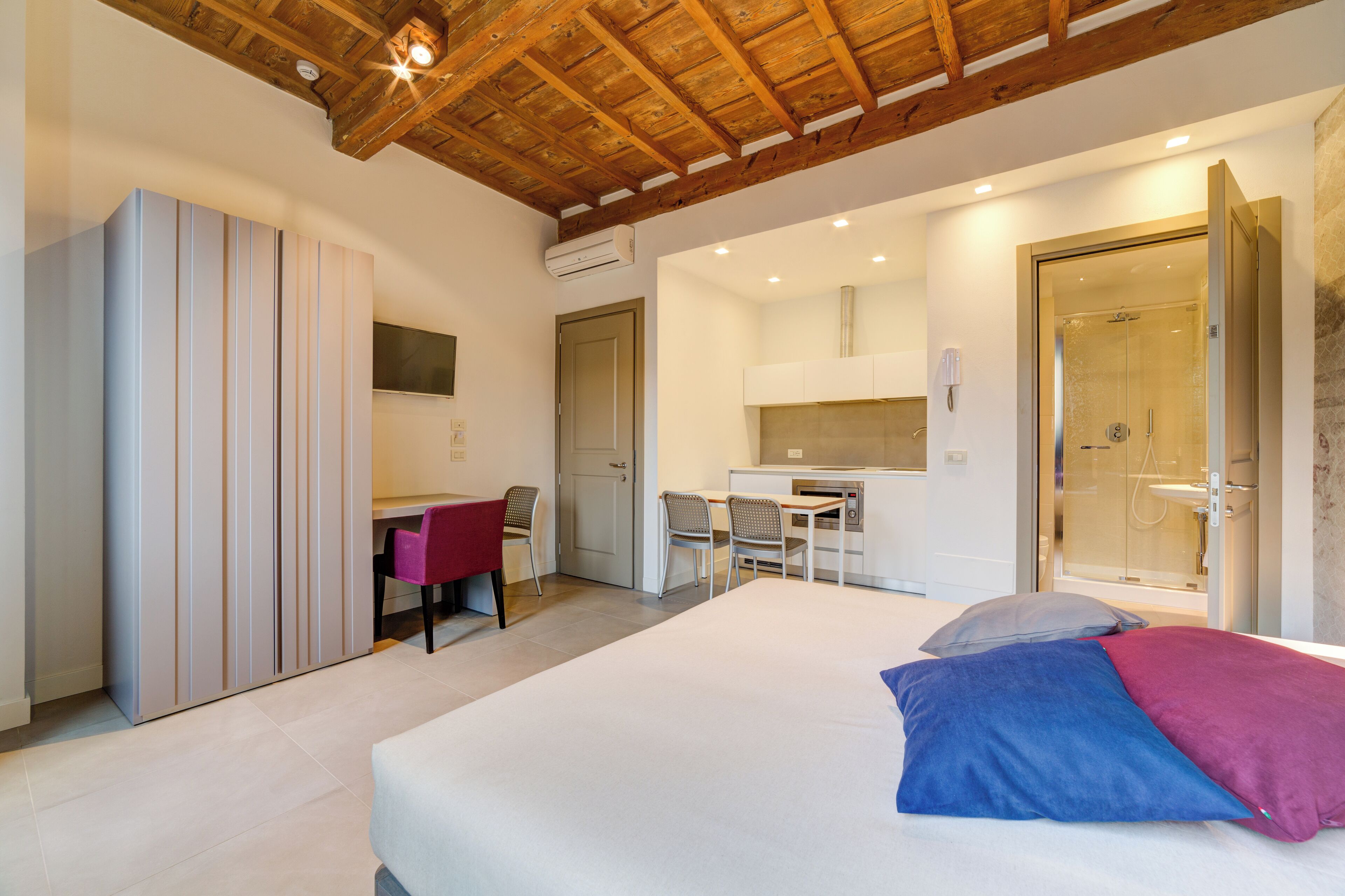 A bedroom with a bed, a desk, and a shower area.