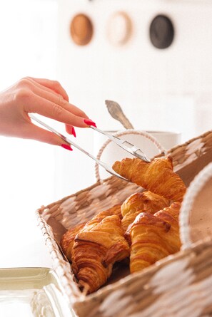 Une main utilisant des pinces pour prendre un croissant dans un panier.