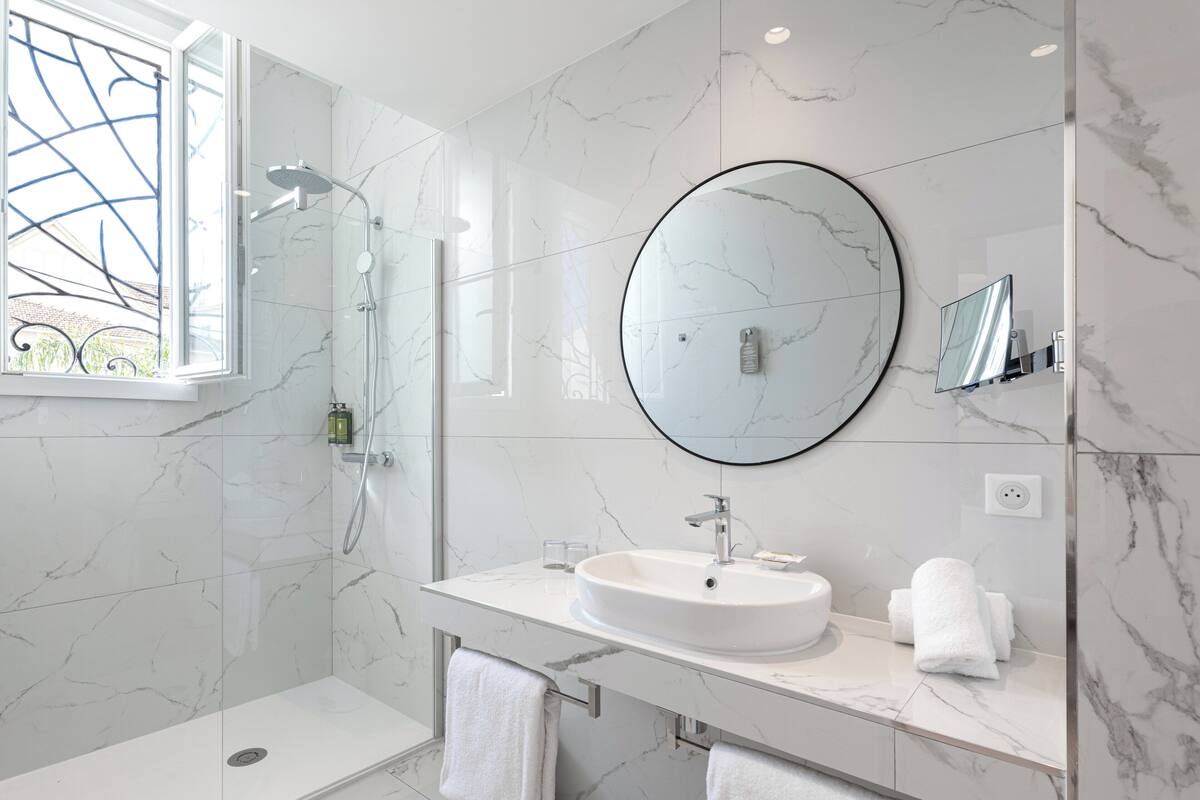 A modern bathroom with a glass-enclosed shower, a round mirror, and a marble-tiled vanity.