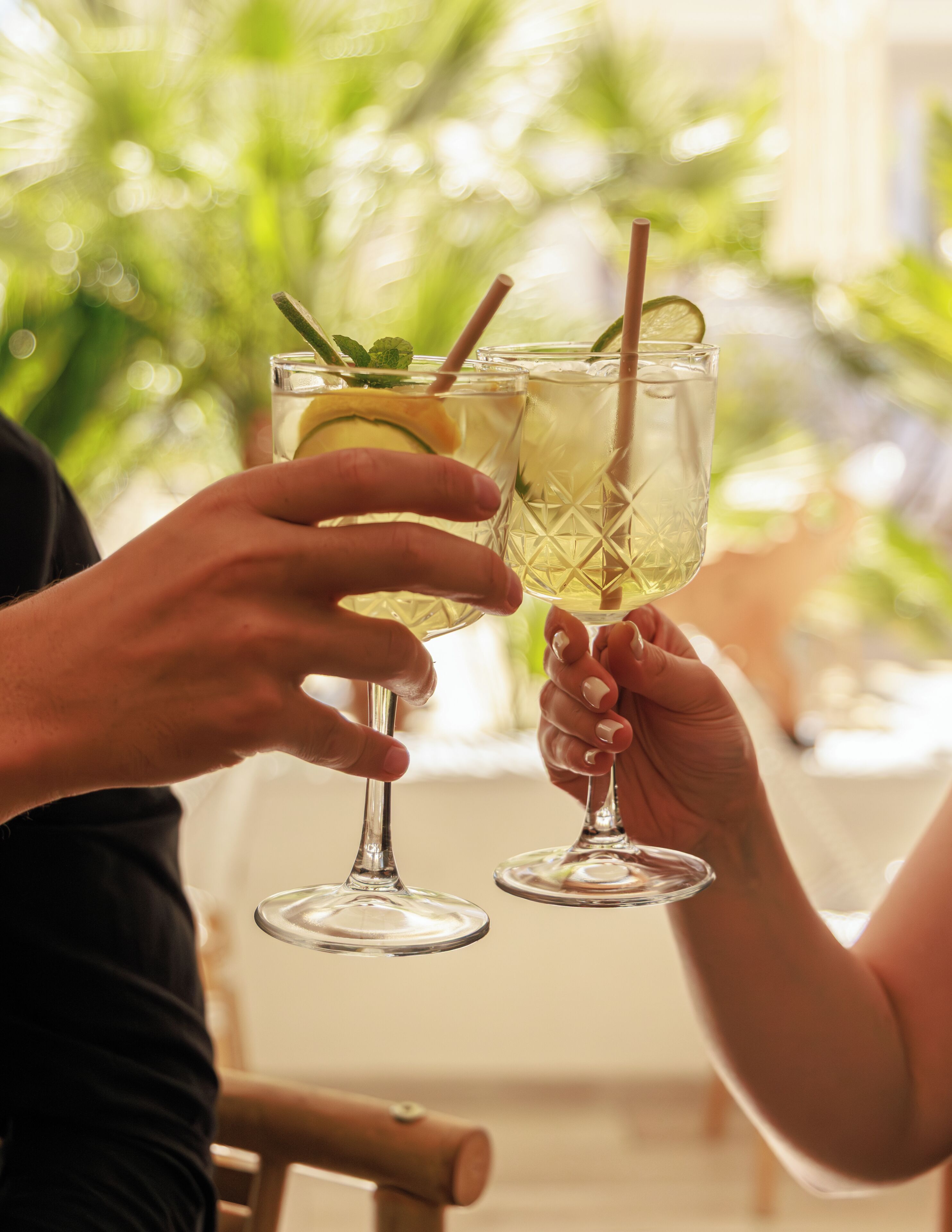 Deux personnes tenant des verres décorés d’une tranche de citron vert et d’une feuille de menthe.