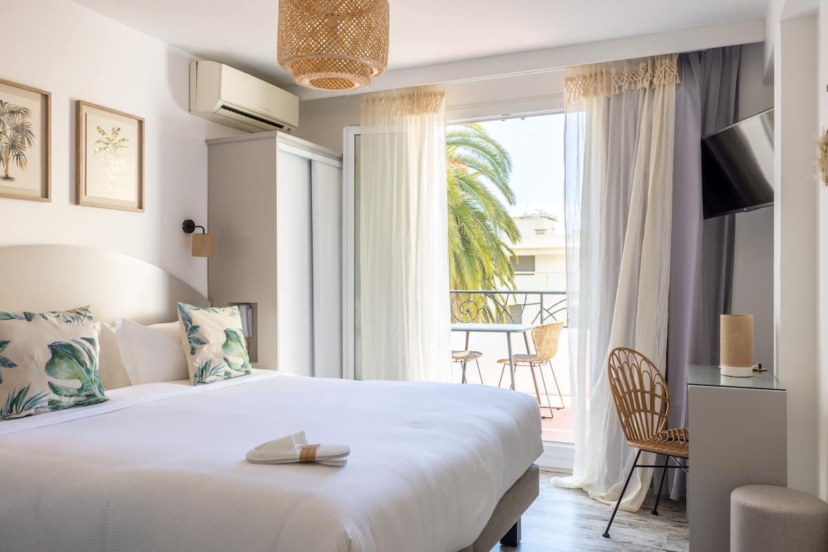 A hotel room with a large bed, a TV, a desk, and a balcony with chairs.