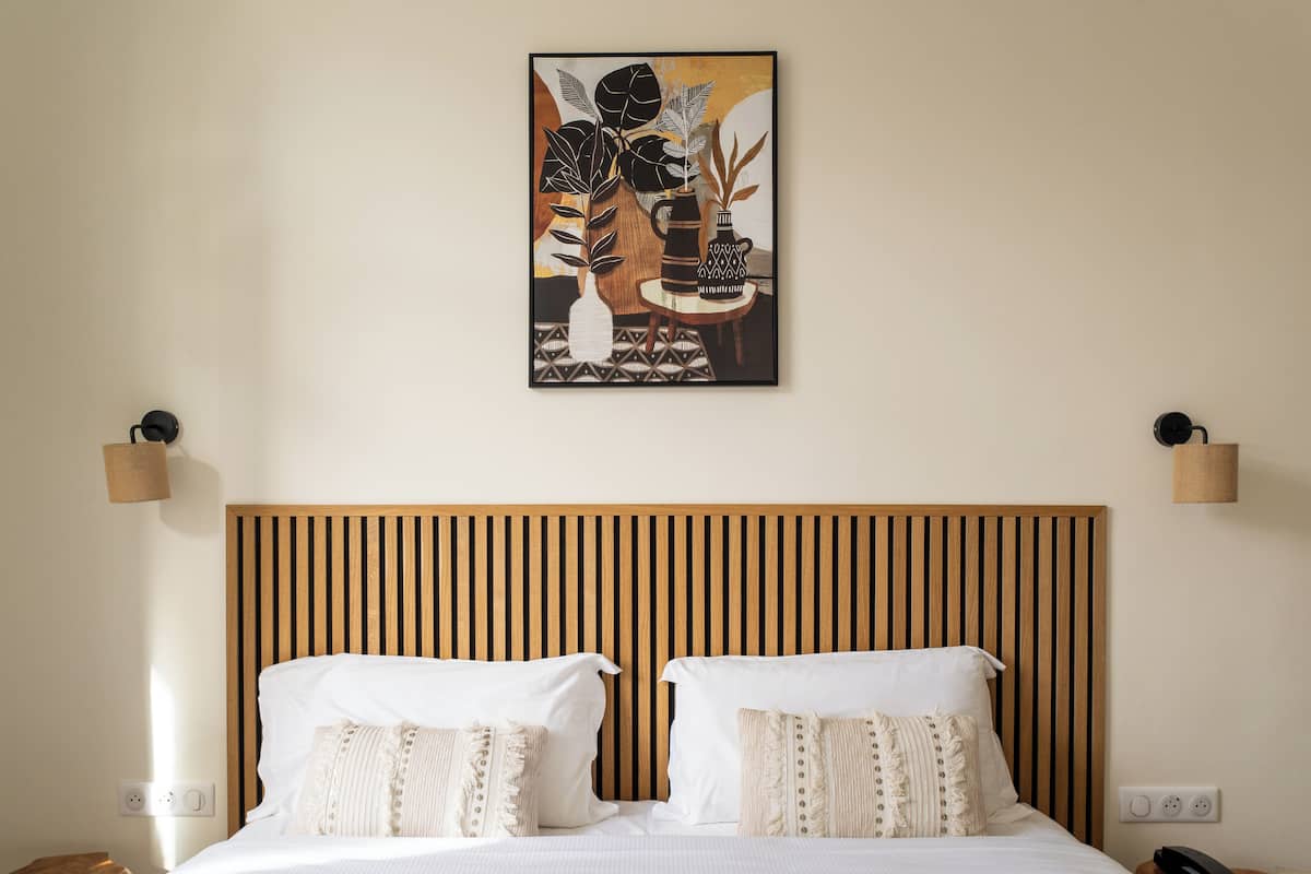 A hotel room with a wooden slatted headboard, white bedding, and a framed artwork above the bed.