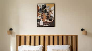 Habitación de hotel con cabecera de madera, ropa de cama blanca y una obra de arte enmarcada sobre la cama.