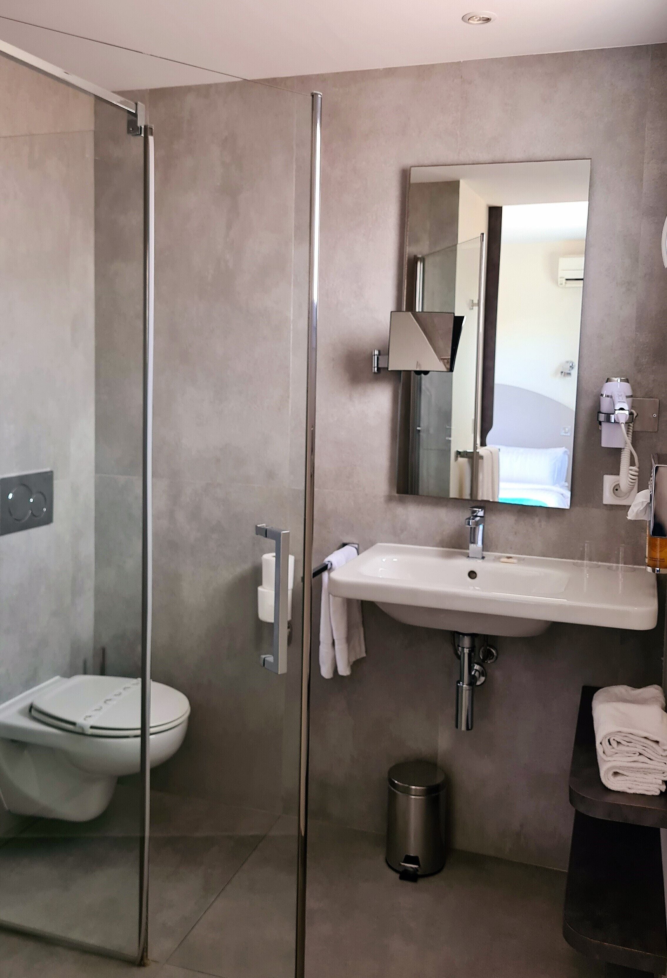 A modern bathroom with a glass-enclosed shower, a white sink, a mirror, and a toilet.