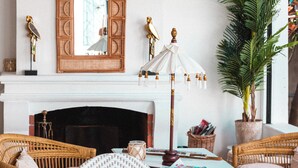 A cozy living room with a fireplace, wicker furniture, a large mirror, and a potted plant. - Hotel La Villa Juan Beach (Antibes)