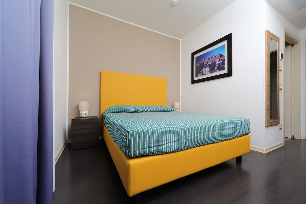 Een slaapkamer met een geel bed, een nachtkastje, een ingelijste foto aan de muur en een spiegel.