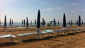 A beach with rows of sun loungers and umbrellas, some occupied by people. - Hotel Anapaya (Lignano Sabbiadoro)