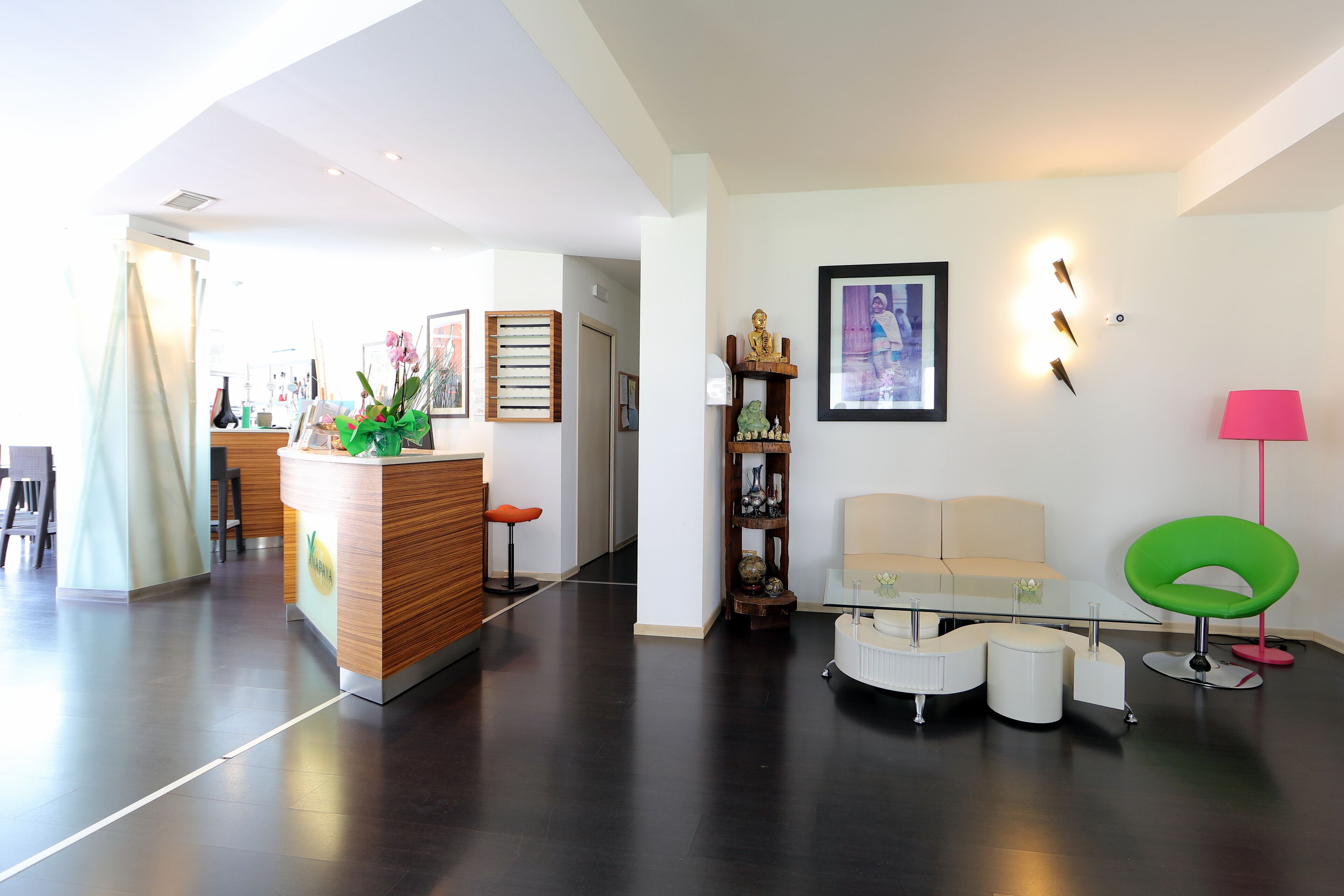 A modern living area with a reception desk, a sofa, a glass table, and a green chair.