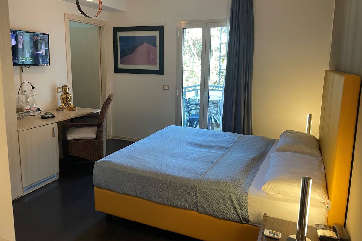 Een hotelkamer met een bed, een bureau met een computer, een stoel, een televisie en een raam met uitzicht op het landschap.