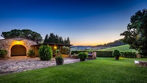 Un arco de piedra que da acceso a un patio cubierto con plantas en macetas y vistas a un viñedo al fondo.