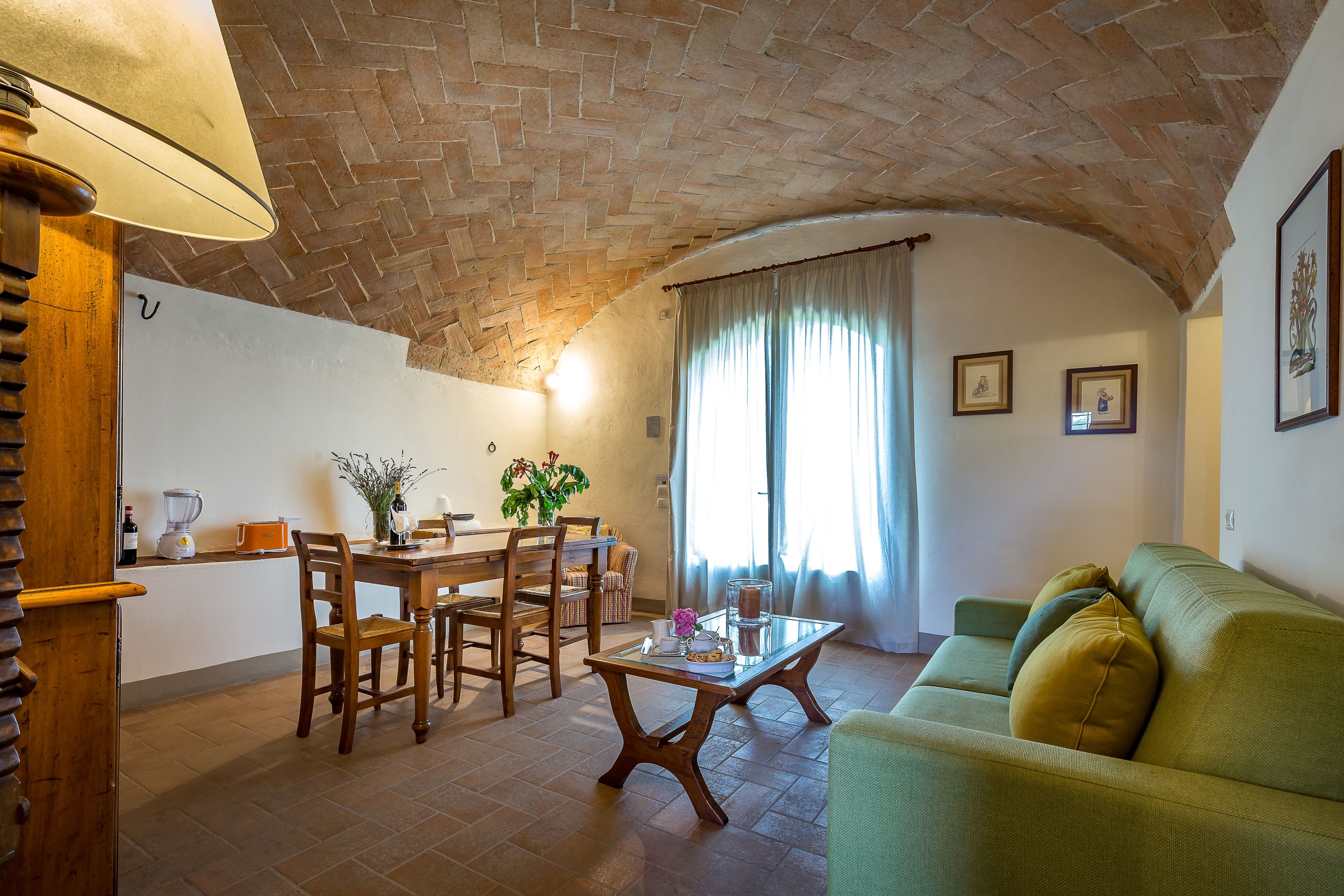 A cozy living room with a brick ceiling, a dining area with wooden furniture, and a green sofa.
