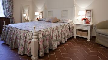Um quarto com edredom floral, cabeceira branca, mesa de cabeceira com abajur e uma cadeira.