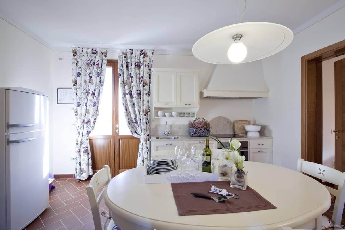 A dining area with a round table, chairs, a white cabinet, a kitchen area with a sink, and a refrigerator.