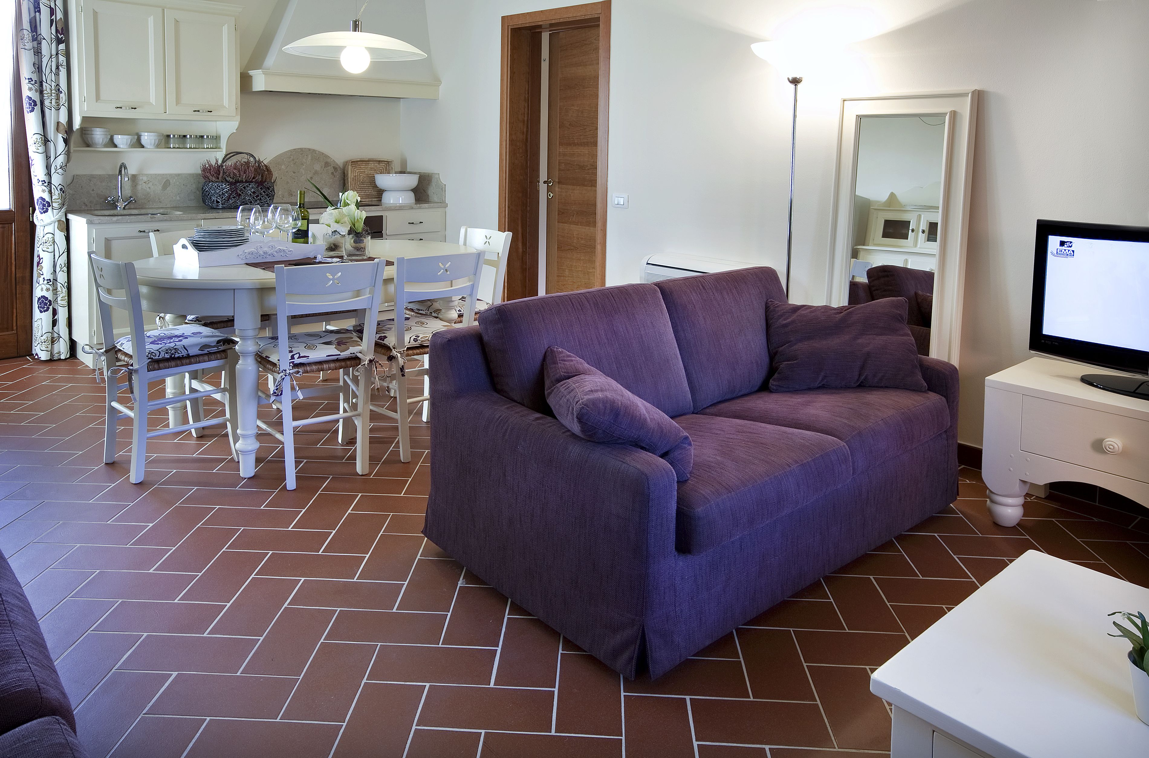 Een woonkamer met een paarse bank, een eettafel met stoelen en een tv op een dressoir.