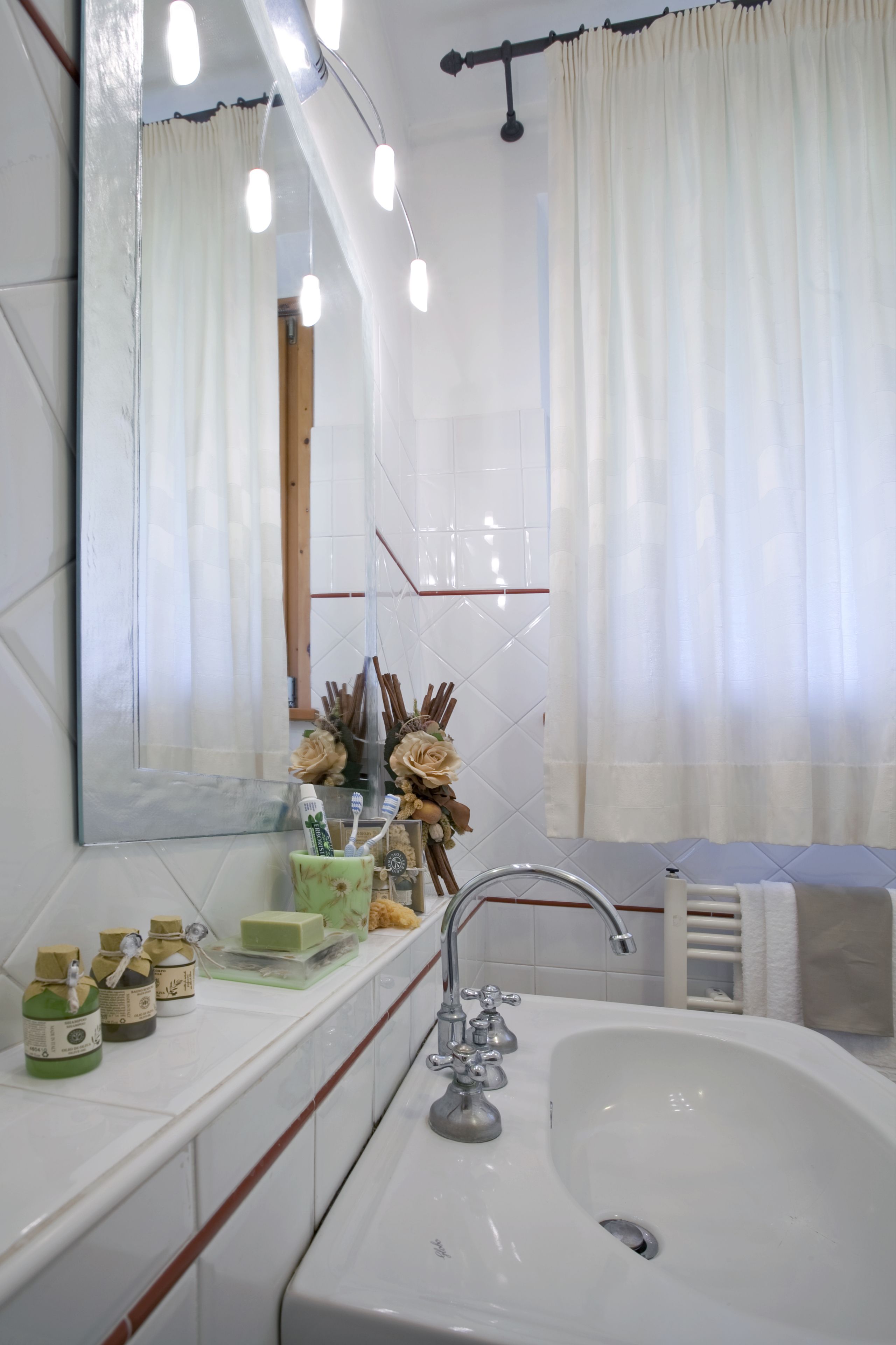 Un baño con lavamanos blanco, espejo y tocador con artículos de aseo.