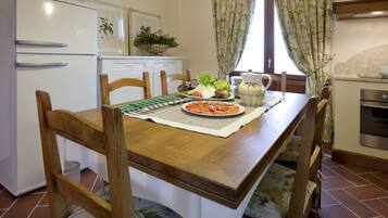 Una cocina con una mesa de madera, sillas, un refrigerador, un lavamanos y una ventana con cortinas.