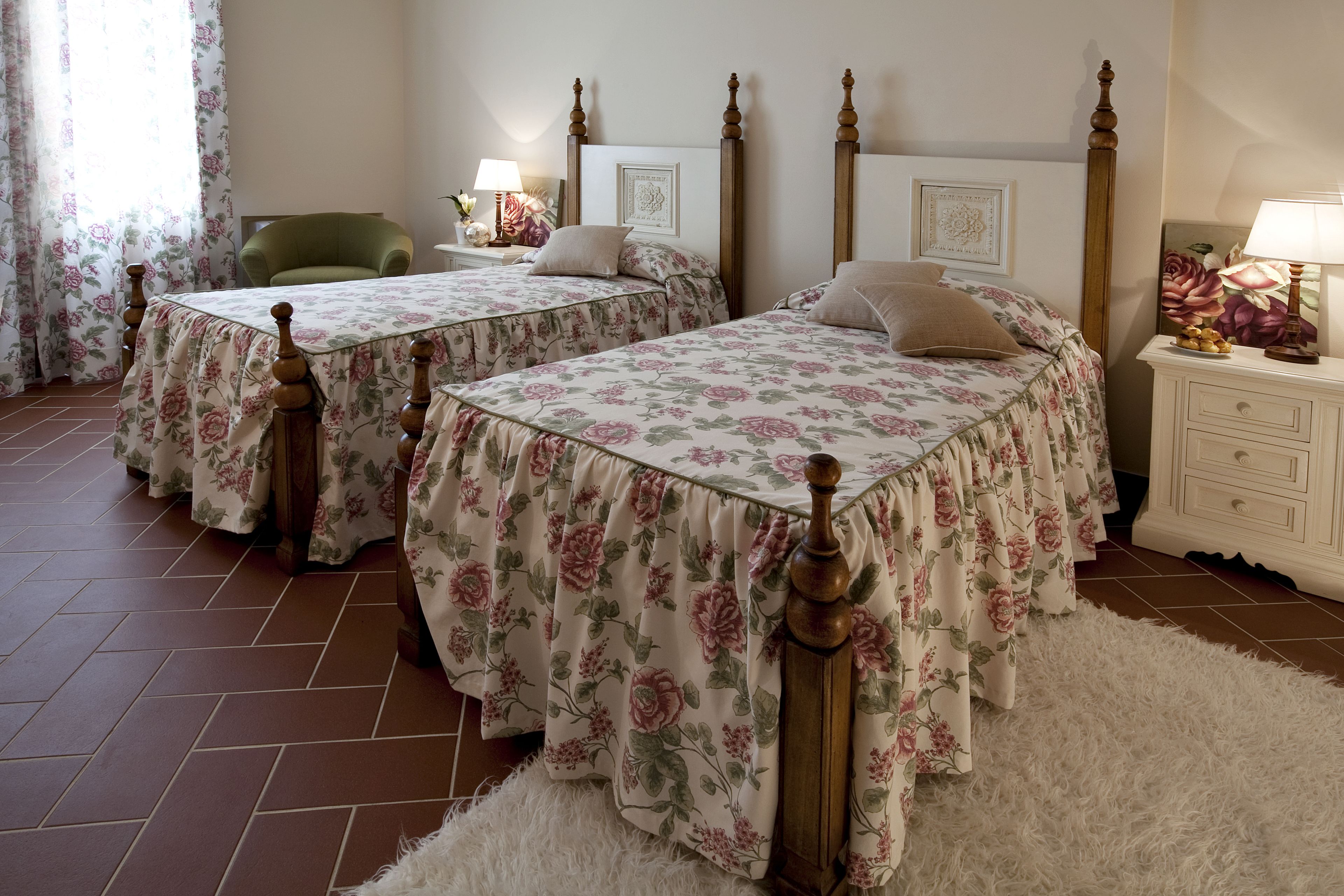 A bedroom with two beds, a green armchair, a white dresser, and a fluffy rug.