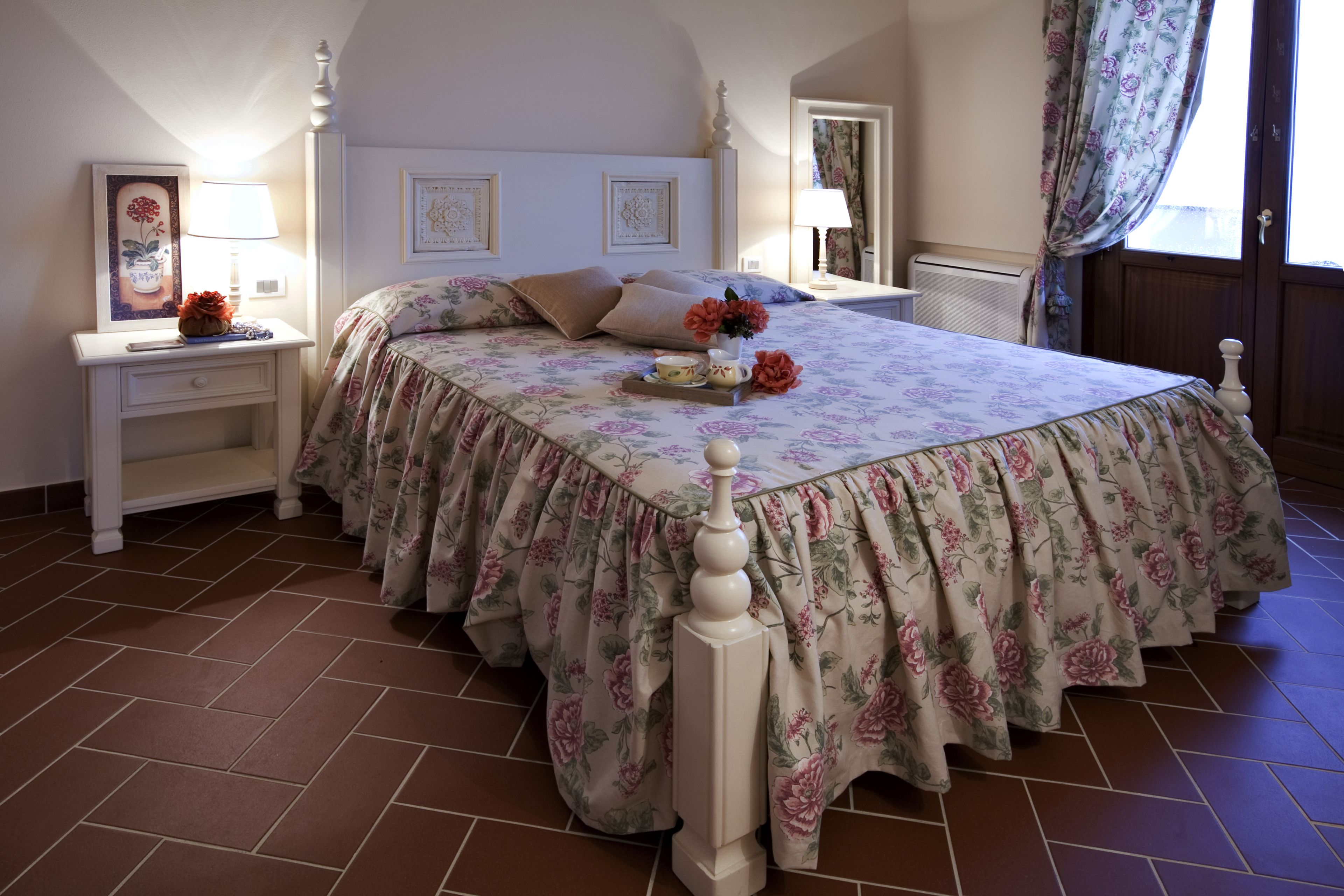 Ein Schlafzimmer mit Blumenmuster-Bettdecke, einem Nachttisch mit Lampe und einer Kommode.