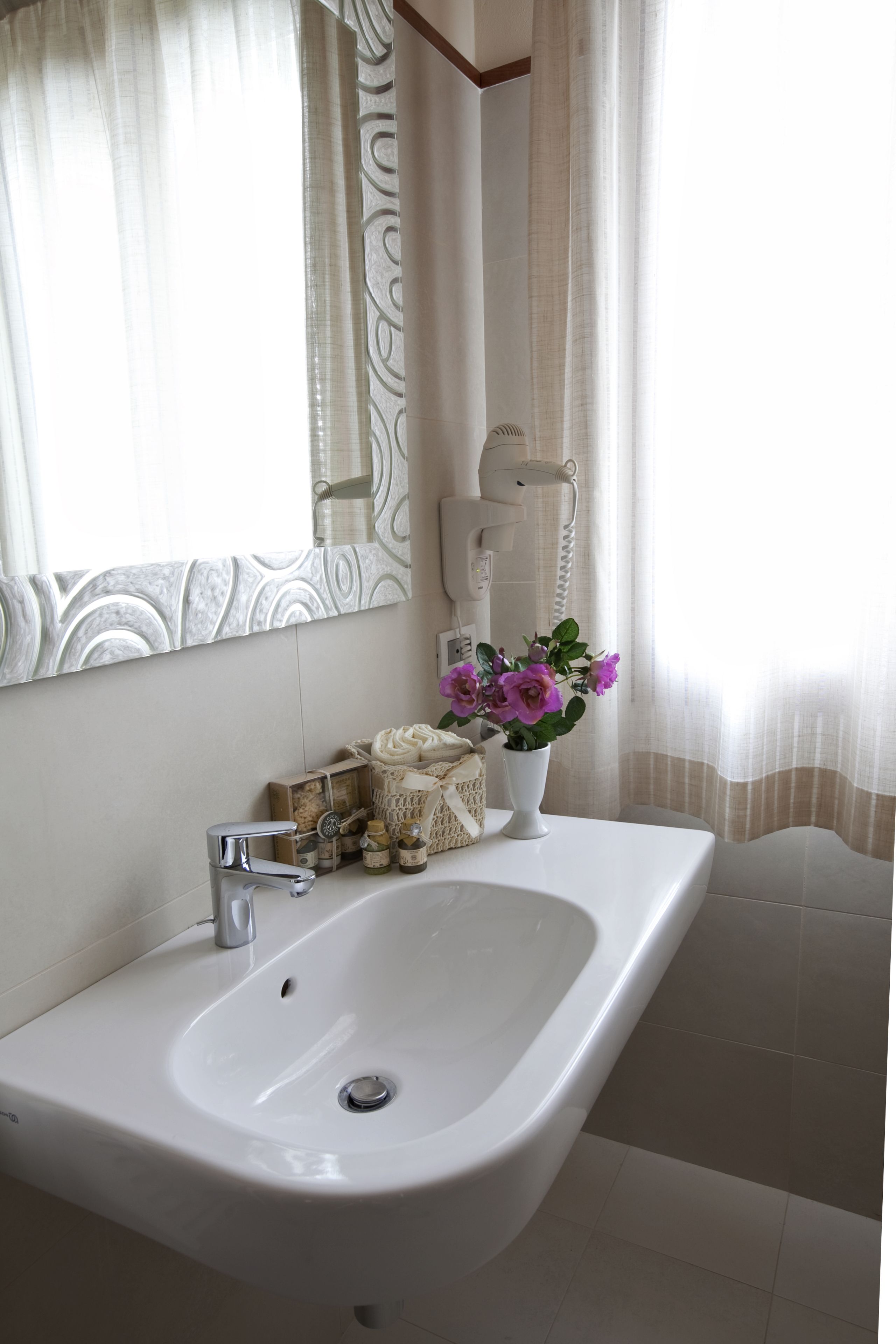 Een badkamer met een wit wastafelmeubel, een spiegel en een vaas met bloemen.