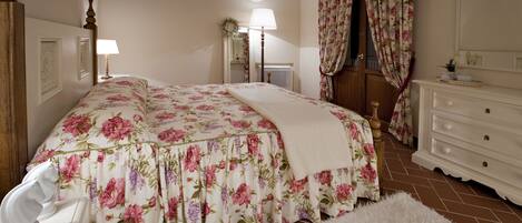 A bedroom with a floral bedspread, a white dresser, a mirror, and a white chair.
